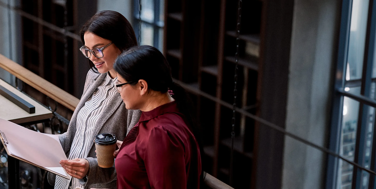 Two female advisors talking while looking at documents while standing in an office