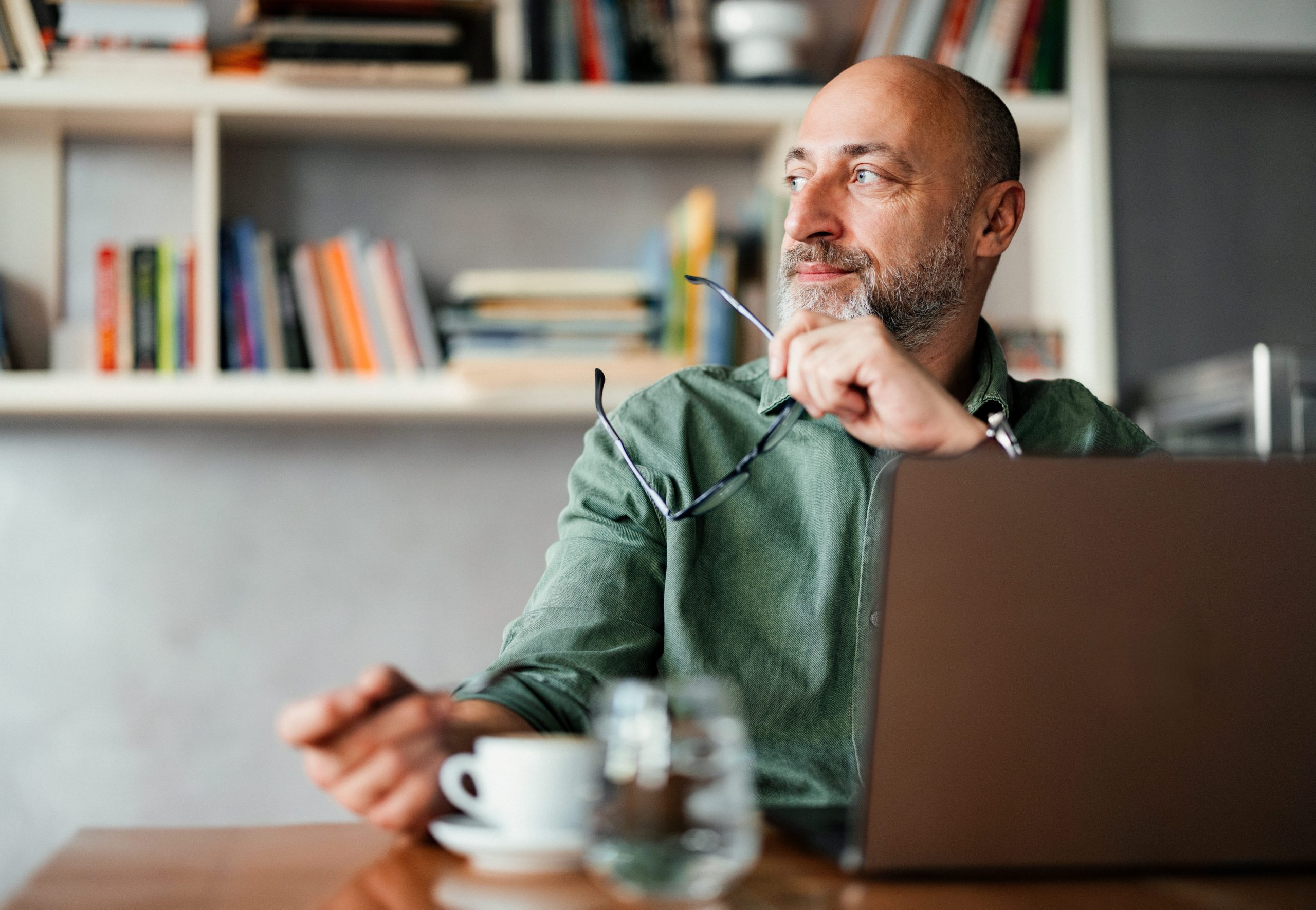 Professional man working on a laptop in a cozy home office with stylish decor and bookshelves.