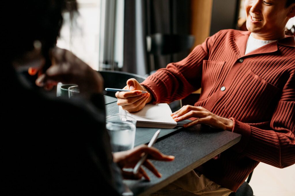 Two people taking notes during a one on one meeting