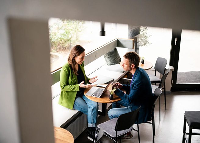 Woman explaining a concept while looking at computer across a cafe table from a man