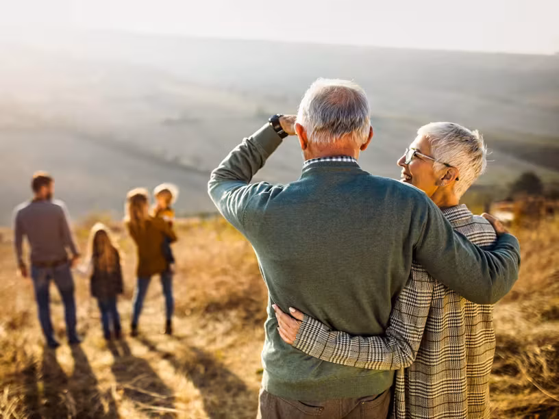 Back view of embraced grandparents enjoying while looking at their family on a hill in autumn day.