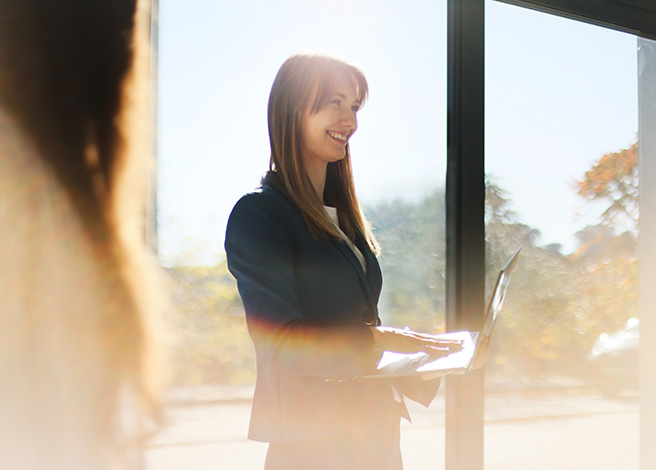 Businesswoman working with laptop against sun in office